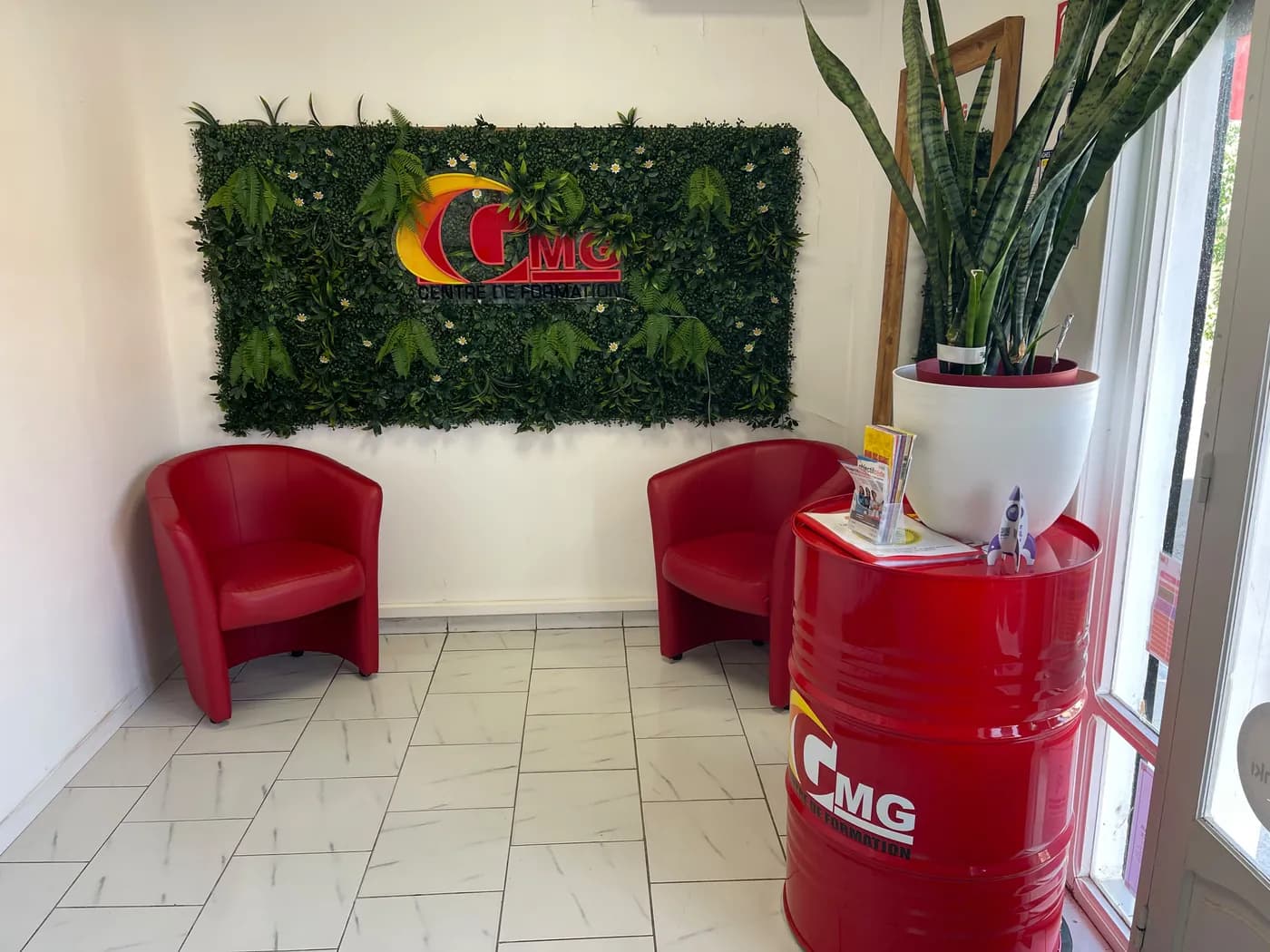 Accueil de Capesterre-Belle-Eau : enseigne GMG sur le mur végétal, fauteuils rouges et fût aux couleurs de l’auto-école